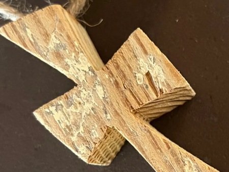 Wooden cross ornament with a rustic finish, showcasing natural grain and texture against a dark background.
