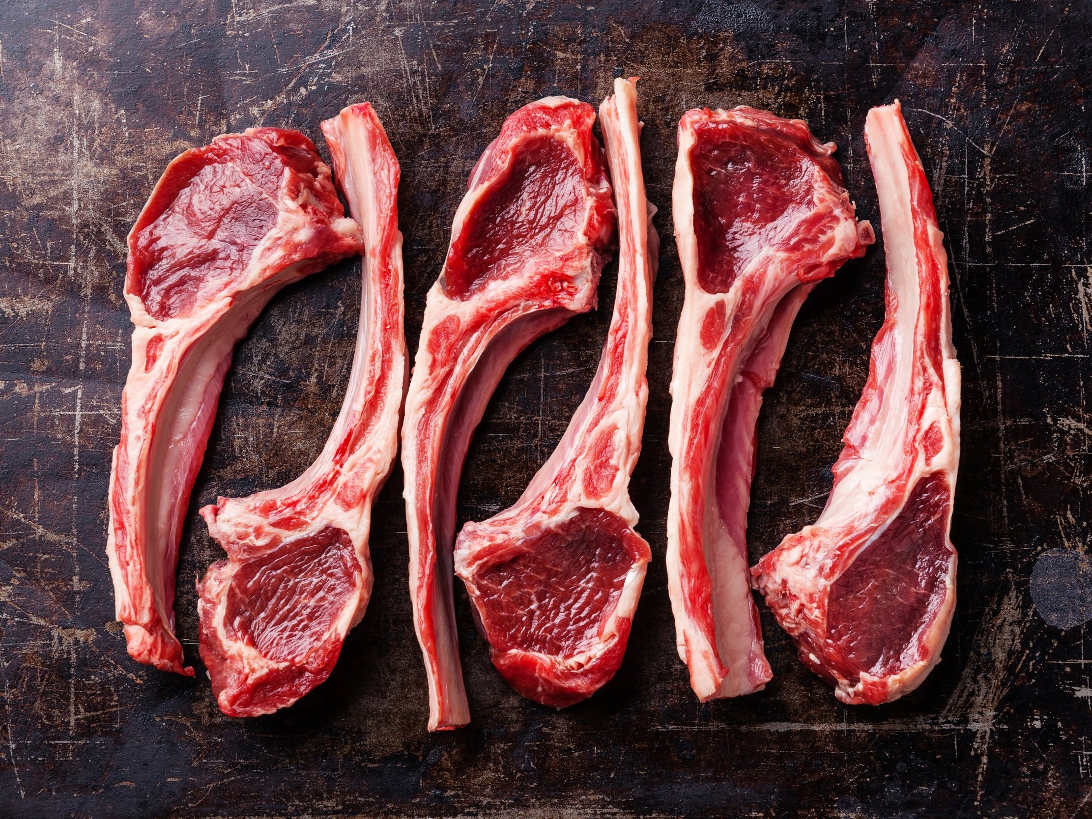 Raw lamb chops arranged on a rustic wooden cutting board, showcasing their marbled red meat and pink fat. Ideal for grilling or roasting, these cuts highlight the quality and freshness of the meat.